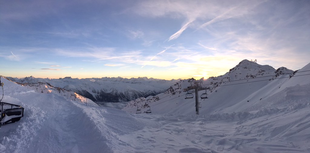 Golden sunset over the Aiguilles d'Arves and Cime Caron seen from Col Rosaël in Orelle, with a snowgroomer preparing the Mauriennaise red slope next to the chairlift.