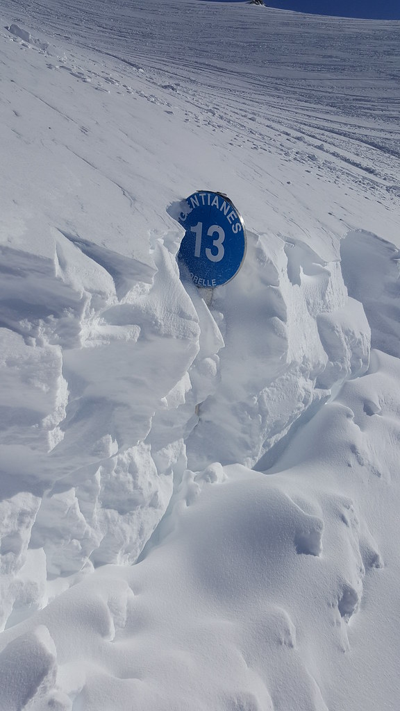 Snow-covered blue slope marker board number 13 on the Gentiane ski run starting from Col Rosaël in Orelle, indicating heavy winter snowfall.