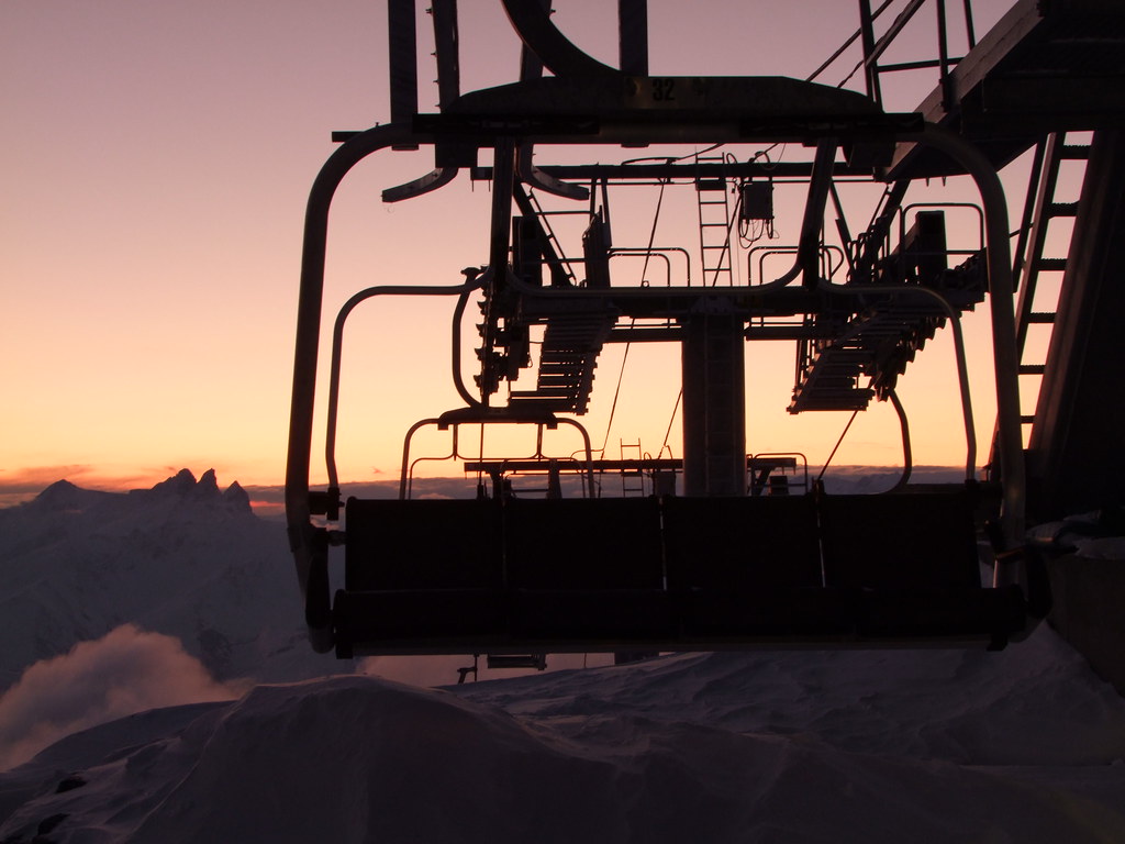 Night falling over a chairlift arrival station in Orelle, with the dark silhouettes of the Aiguilles d'Arves against a deep blue dusk sky.