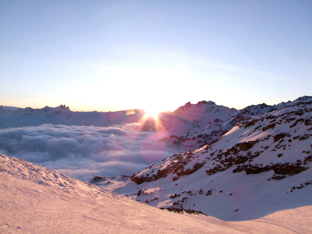 Golden hour sunlight clipping the mountain peaks on the Bouchet ski run in Orelle, with a sea of clouds hiding the valley below at the end of the day.