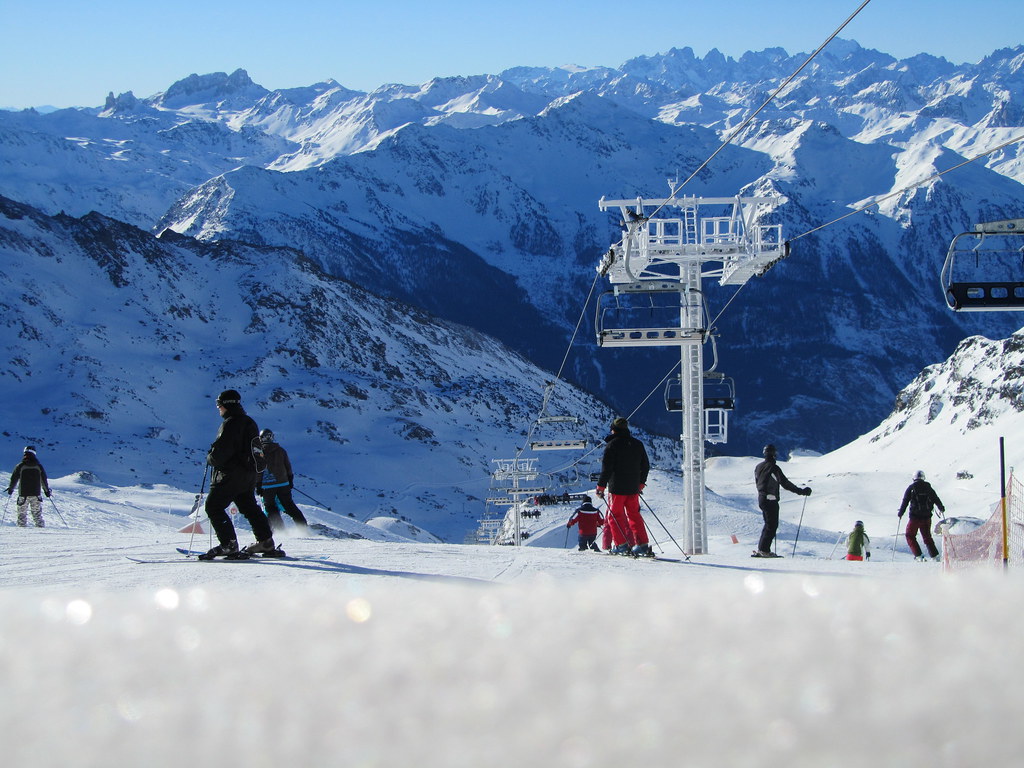 Low-angle ground-level shot of fresh snow as skiers drop down the Mauriennaise slope under the Col de Rosaël chairlift in Orelle at the end of the day.