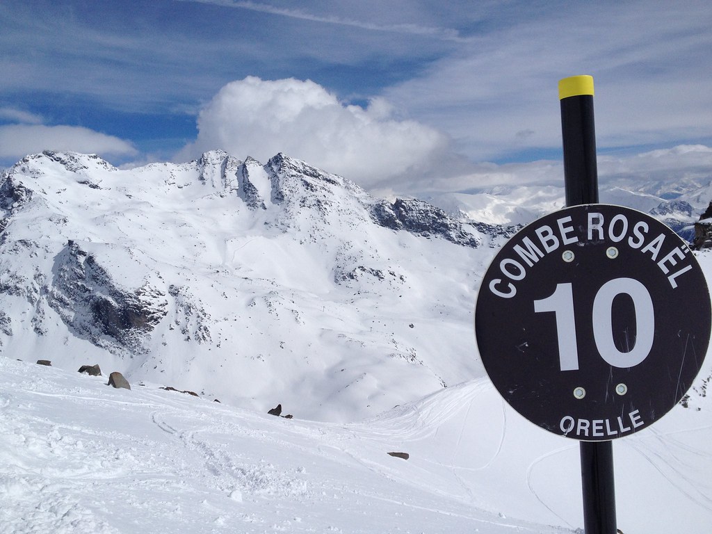 Panoramic view from Combe Rosaël black slope in Orelle with marker sign number 10 on the right, showing distant peaks, Col du Bouchet, and Coraïa, Peyron, and Croix d'Antide runs.