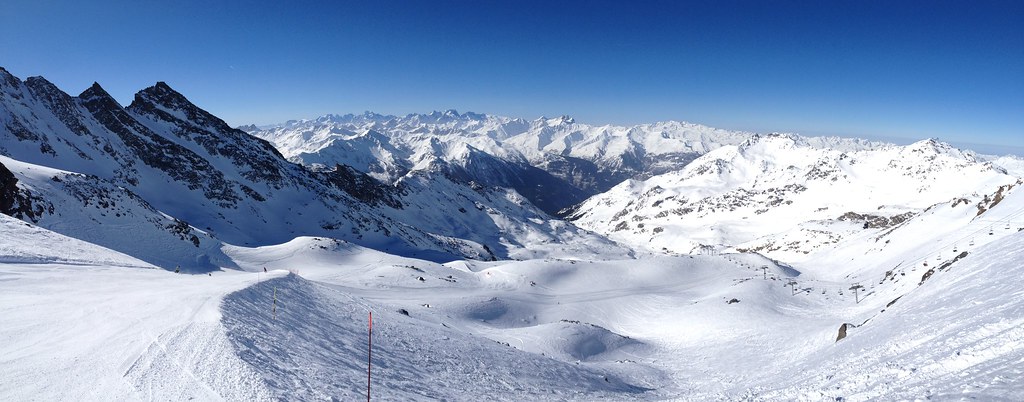 Panoramic view from the Coraia red slope starting from Col du Bouchet at 3230m in Orelle, with crisp white snow, clear blue sky, and endless jagged alpine peaks.