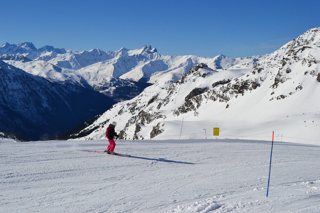 Female skier on the Croix d'Antide slope in Orelle with panoramic background views of the Aiguilles d'Arves and the Bonrieu torrent valley.