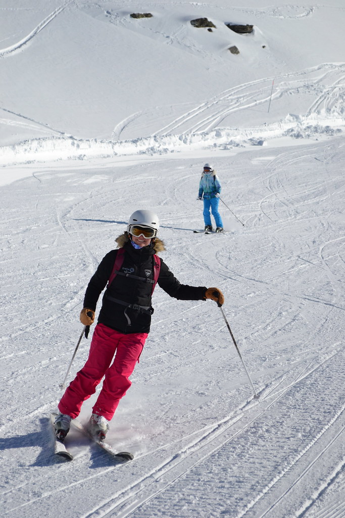 wo smiling skiers enjoying a relaxed run on a sunny, snow-covered slope in Orelle under a bright blue sky.