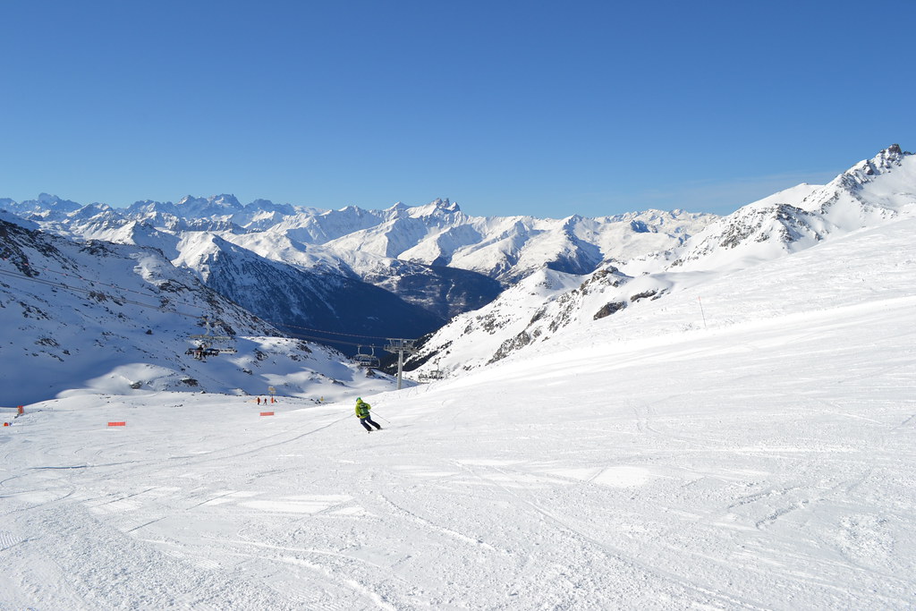 Panoramic view at the intersection of Peyron and Croix d'Antide slopes in Orelle under a clear blue sky, featuring wide open runs and mountain views.