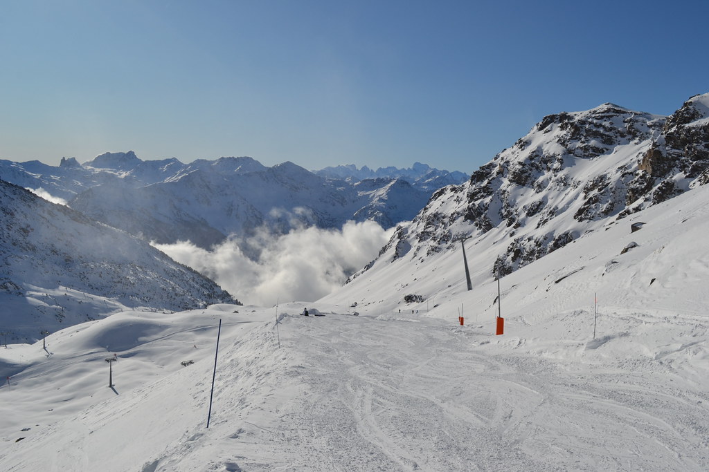 Scenic narrow trail on the Gentianes run above the steep Mauriennaise slope in Orelle, with crisp white snow, blue sky, and mountain panoramas.