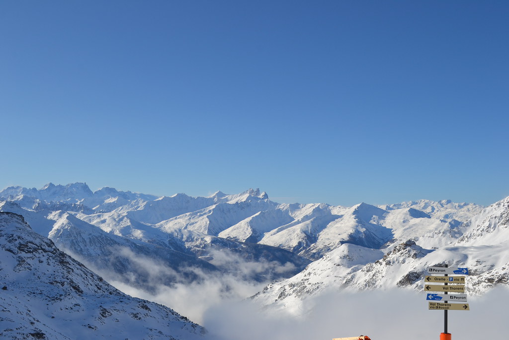 Panoramic view below the Bouchet chairlift bottom station in Orelle showing ski direction signs pointing toward Orelle, Val Thorens, and Col Rosaël.